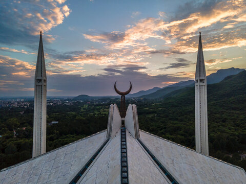 Aerial view of Faisal Masjid with its iconic minarets and crescent moon symbol overlooking the lush Margalla Hills under a dramatic sunset sky Islamabad, Islamabad Capital Ter, Pakistan.