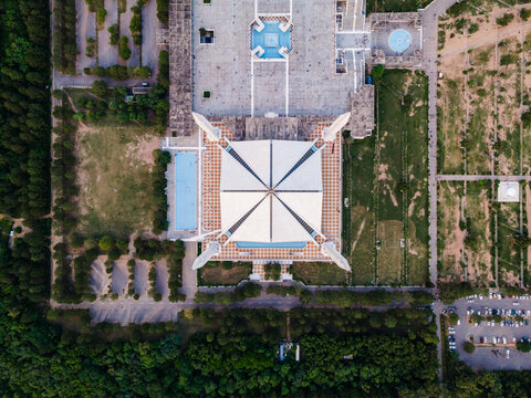 Aerial view of Faisal Masjid with its iconic white triangular roof and four minarets surrounded by green landscapes and parking lots in Islamabad, Islamabad Capital Ter, Pakistan.