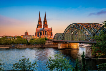 Fototapeta premium Beautiful summer sunrise view of the cityscape of Cologne, Germany, with Cathedral and Hohenzollern Bridge in golden morning sunlight