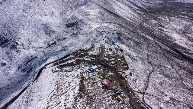 Aerial view of Babusar Pass with snow-covered mountain peaks, a winding road, and small buildings in Babusar, KPK, Pakistan.