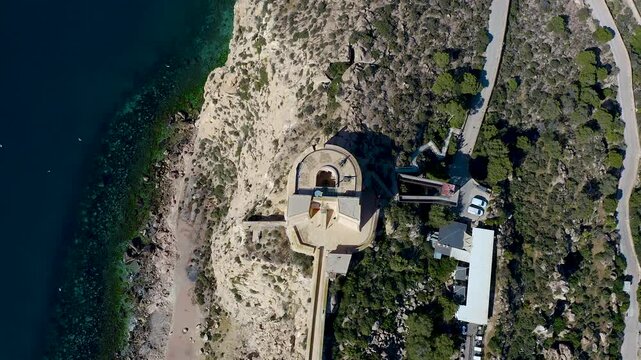 Stunning drone shot of the coastal city of Aguilas in Spain, highlighting the San Juan de las Aguilas Castle fortress on the cliff and the beautiful Poniente Bay beach. 