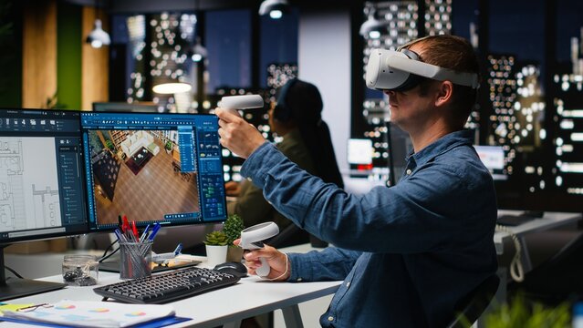 Male engineer using VR headset and AI on interior design software at workstation, moving assets for apartment layout with artificial intelligence suggestions in 3D render program. Camera B.