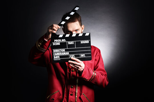 Professional actor in suit with clapperboard on black background with spotlight
