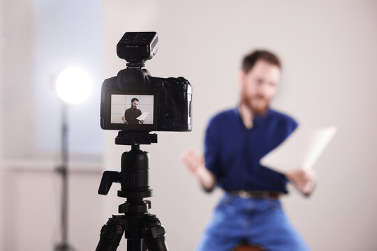 Actor with script rehearsing against light grey background, focus on camera