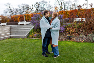 Fototapeta premium Couple shares warmth in a garden during autumn season with colorful trees in the background
