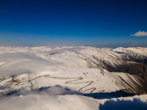 Aerial view of the winding road of Babusar Pass through snow-covered mountain peaks under a clear blue sky in Babusar, KPK, Pakistan.