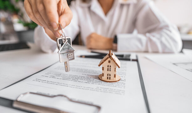 Woman real estate agent gives keys paperwork and miniature house model. Concept of buying apartment, rental contract signing, trusted agency service and modern housing ownership.