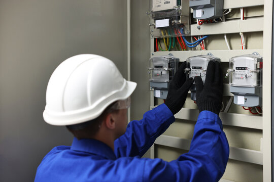Electrician checking fuse box with electrical meters indoors