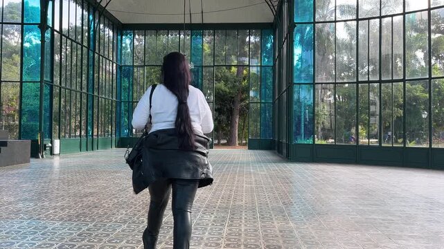 Woman walking inside elegant glass pavilion in urban park  in Petropolis, Brazil  look down camera full long shot