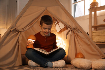 Little boy reading book in toy wigwam at home © New Africa