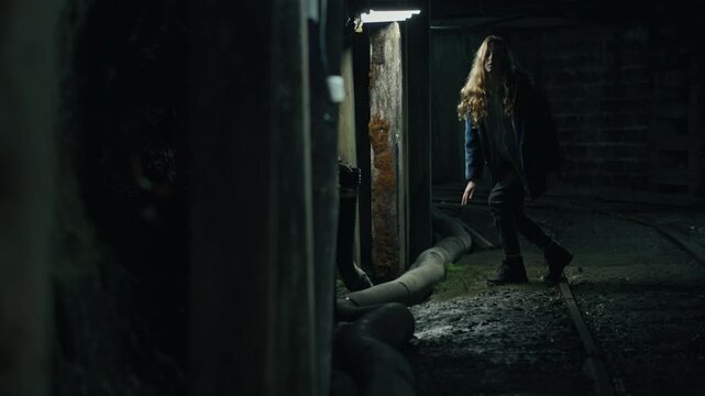 Scared young girl getting up and running away in a dark, abandoned industrial basement