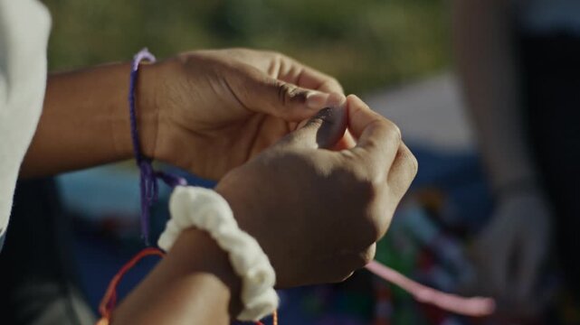 Close up of hands weaving colorful threads into a friendship bracelet, representing handmade craft