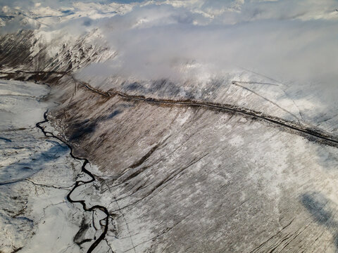 Aerial view of Babusar Pass winding through snow-covered mountain slopes with a river in the valley under a cloudy sky Babusar, KPK, Pakistan.