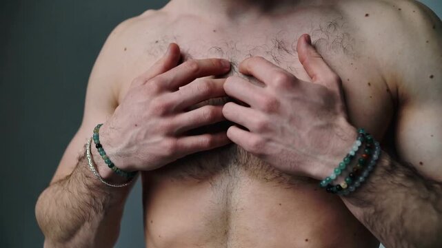 Young man with hairy chest touching skin, wearing stone bead bracelets, close up shot