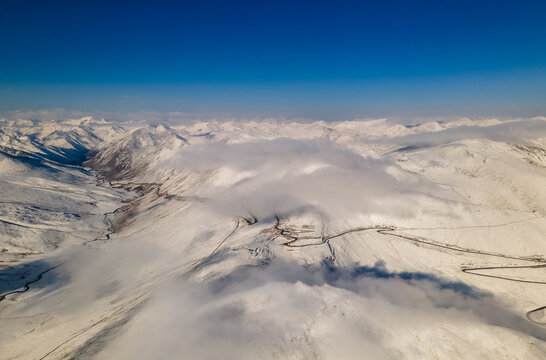 Aerial view of Babusar Pass winding through snow-covered mountain peaks under a clear blue sky with low clouds Babusar, KPK, Pakistan.
