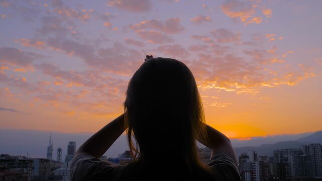 Silhouette of woman is lifting hands up, doing stretching and yoga exercises against the cloudy sky at sunset or sunrise - sun salutation. Fitness, sport, freedom and outdoor activity concept