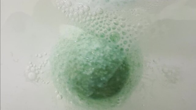 Green bath bomb whirls and fizzes in bathtub water