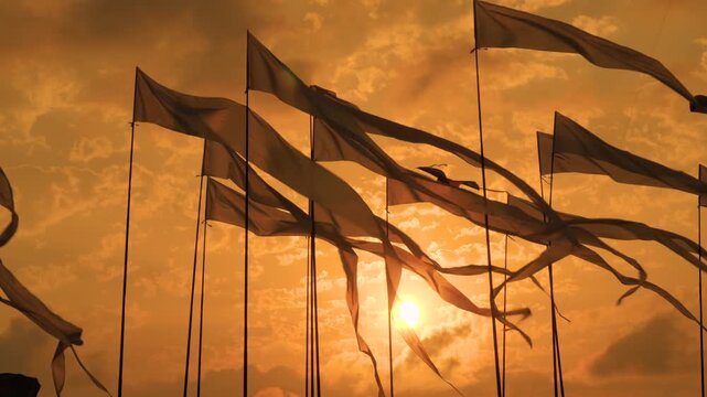 Silhouettes of decorative flags are fluttering in the wind against the dramatic sunset sky at the outdoor city festival. Freedom, entertainment, summer and celebration concept