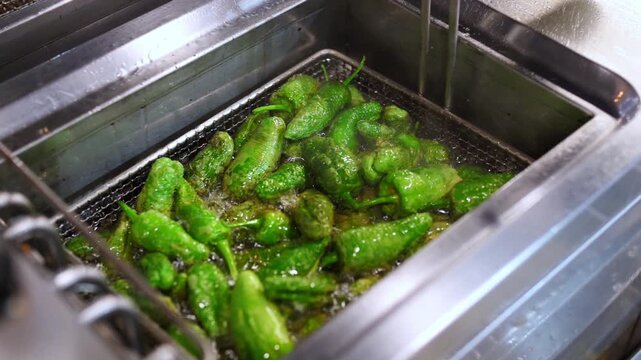 Close up of traditional spanish pimientos de padron sizzling in a deep fryer basket, a popular appetizer prepared in a restaurant kitchen