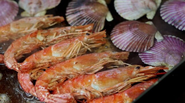 Assorted fresh seafood, including prawns, scallops, and clams, sizzling on a hot grill. Delicious shellfish cooking in a restaurant kitchen