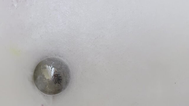 Overhead shot shows soapy water getting sucked down bathtub drain