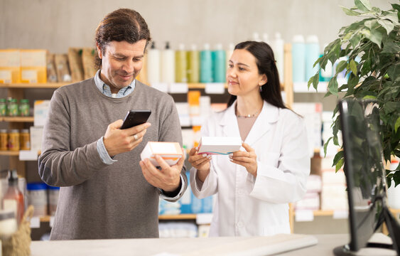 Positive middle-aged man scanning QR on pills box while pharmacist consulting him in chemistry
