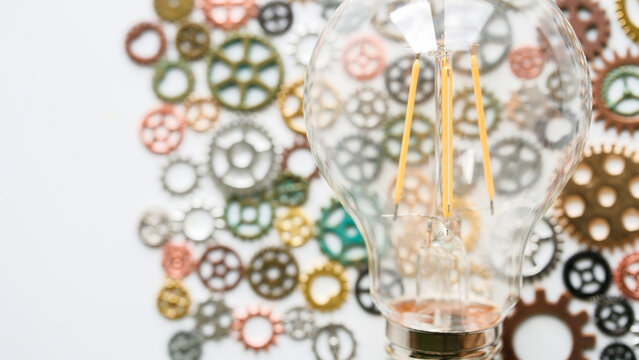 Transparent LED light bulb placed over various metallic cogs and gears. Ideal template for business innovation, brainstorming, and technological evolution concepts. Photo