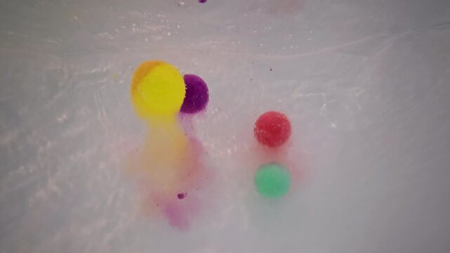 Underwater POV shows colorful bath bombs plunging into bathwater