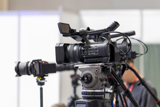 Digital camcorder on a heavy duty tripod in a spacious exhibition center. Modern recording gear for corporate video production and media news