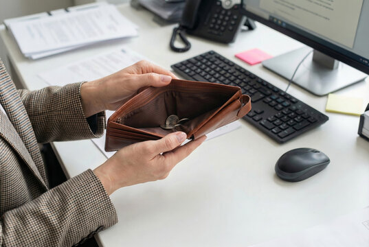 Conceptual image of a woman in business suit holding an empty leather wallet with few coins over an office desk. Symbol of inflation, economic crisis, financial struggle and reduced purchasing power
