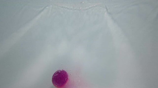 Underwater POV shows purple bath bomb plunging into bathwater