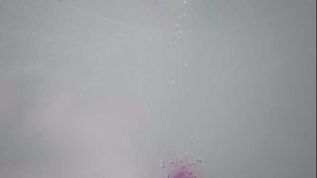 Underwater POV shows multiple bath bombs dropping into bathtub water