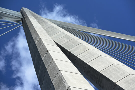A dramatic low-angle photograph of a modern cable-stayed bridge pylon with steel cables stretching into a blue sky