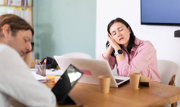 Tired adult man and woman colleagues falling asleep while working with tablet and laptop in office