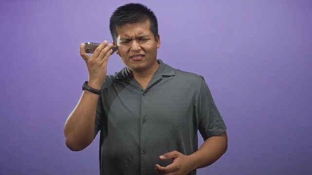 Man holds smartphone to his ear, eyes closed and wincing while tapping the handset and checking sound, shot in a studio; frustration.