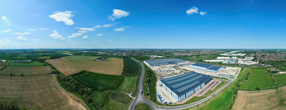 Aerial view of Symmetry Park logistics hub featuring large modern warehouses surrounded by green agricultural fields and a road junction in Kettering, England, United Kingdom.