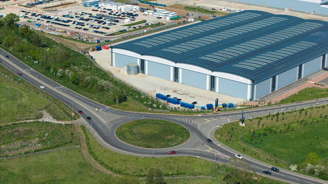 Aerial view of Symmetry Park distribution center featuring a large modern warehouse, a busy roundabout, and extensive parking facilities in Kettering, England, United Kingdom.