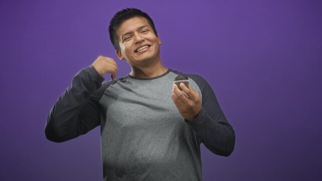 Man holding muffin in hand wipes brow in studio with purple backdrop and casual grey longsleeve raglan shirt; amusement.