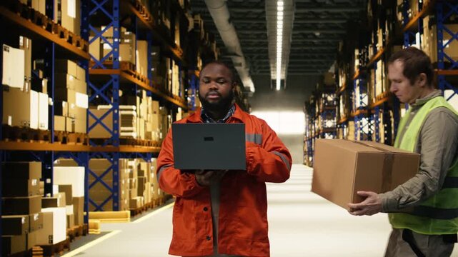 Multiethnic staff members sorting cardboard boxes in industrial storage facility. Two diverse men doing manual labor and checking inventory to ensure safe shipping, global logistics.