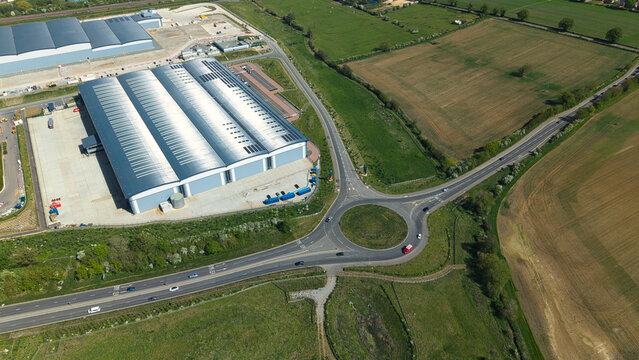 Aerial view of Symmetry Park industrial warehouse and a busy roundabout surrounded by green fields in Kettering, England, United Kingdom.