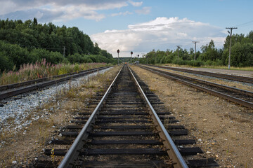 Obraz premium A deserted railway line stretches into the distance. Railroad tracks in the countryside. In the foreground are rails laid on wooden sleepers on a gravel base. In the distance are signal poles.