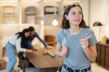 Young European woman stands in a furniture salon and chooses a new kitchen set for her apartment. Customer is considering options for finishing in a furniture store © JackF