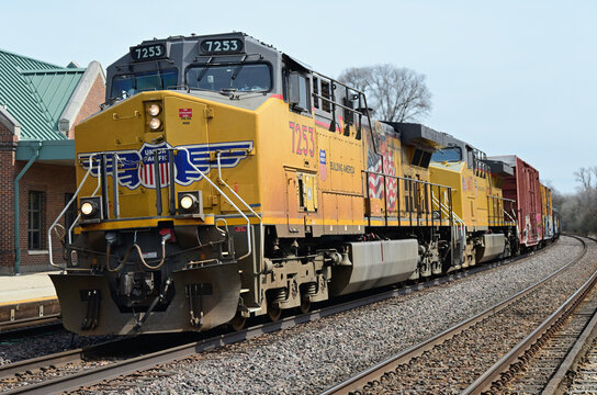 A westbound Union Pacific Railroad freight train passing by a suburban commuter rail station on its westward journey from Chicago.