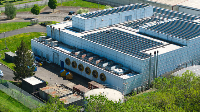 Aerial view of a modern data centre building featuring rooftop solar panels and large industrial cooling fans surrounded by green trees Wellingborough, England, United Kingdom.