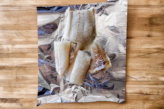 Top view of multiple pieces of raw, uncooked cod fillets or cod fish loins laid on a tinfoil background. Thick, healthy white Atlantic cod fish is being prepared in a restaurant kitchen for frying.