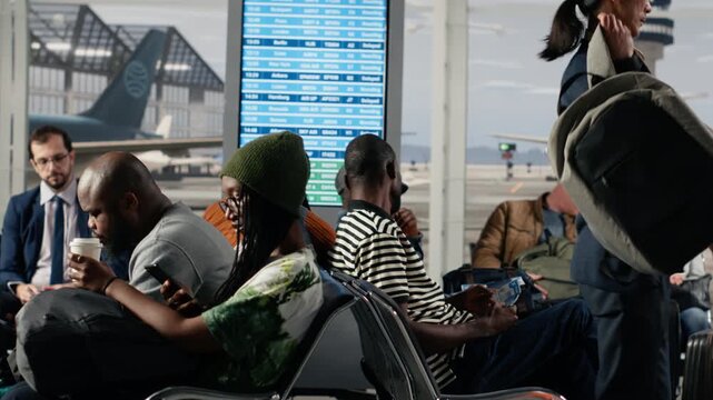 Men and women in airport lounge standing up from chairs for departing airplane flight boarding call. Diverse passengers leaving airport terminal, going to boarding gate with backpacks