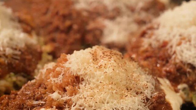 A mouth-watering, cinematic extreme close-up shot capturing the fine texture of freshly grated Parmesan cheese as it rests atop large, steaming Italian meatballs. The meatballs are generously coated i