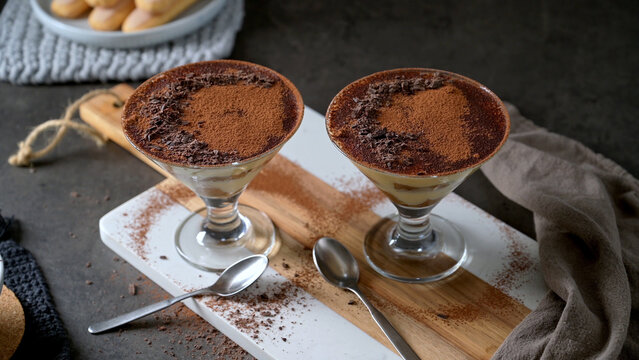 Two glasses of classic Italian tiramisu topped with cocoa powder and dark chocolate shavings