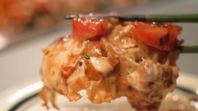 A macro shot of a freshly prepared volcano sushi roll being lifted with chopsticks. The footage highlights the creamy, melted topping of baked seafood and spicy mayonnaise, garnished with vibrant oran