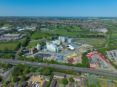 Aerial view of the industrial complex and warehouses with yellow trucks near the A45 road and green fields in Little Irchester, England, United Kingdom.